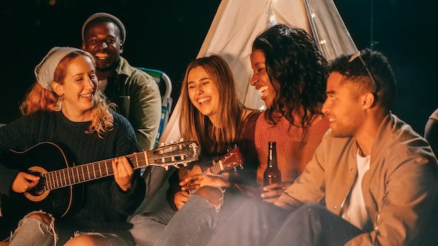Group of friends laughing and playing music around a campfire – representing Gemini’s social, fun-loving, and outgoing personality in relationships