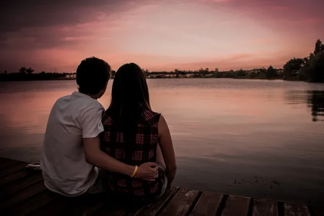 Couple sitting together by a peaceful lakeside at sunset, symbolizing emotional connection, romance, and relationship compatibility often associated with Aries zodiac sign.