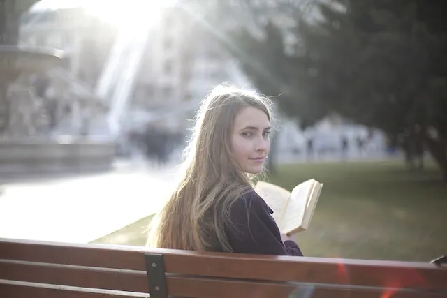 Thoughtful Pisces woman reading on a park bench, reflecting the zodiac sign's intuition, imagination, emotional depth, and quiet, reflective nature.