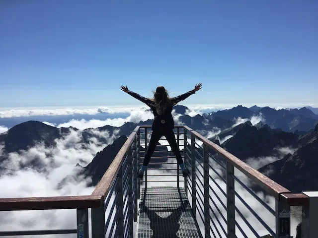 Person standing on a mountain skywalk above the clouds, symbolizing the adventurous, optimistic, and freedom-loving personality of Sagittarius.